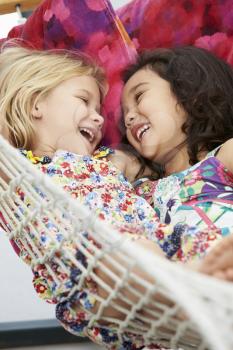 Two Young Girls Relaxing In Garden Hammock Together
