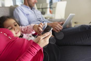Family On Sofa With Smartphone, Laptop And Digital Tablet