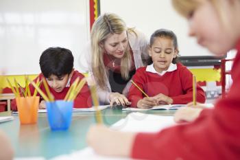 Teacher Helping Female Pupil With Writing Reading At Desk