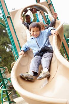 Young Boy Playing On Slide In Playground