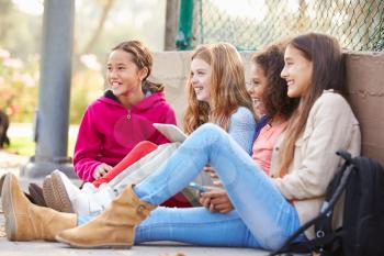Young Girls Using Digital Tablets And Mobile Phones In Park