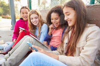 Young Girls Using Digital Tablets And Mobile Phones In Park