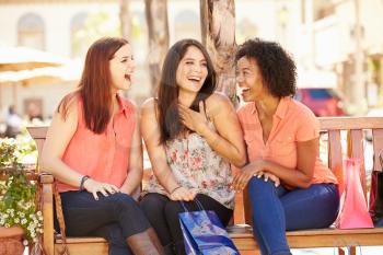 Three Female Friends With Shopping Bags Sitting In Mall