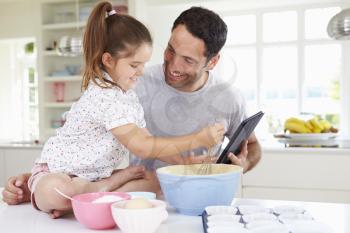 Father And Daughter Following Cake Recipe On  Digital tablet