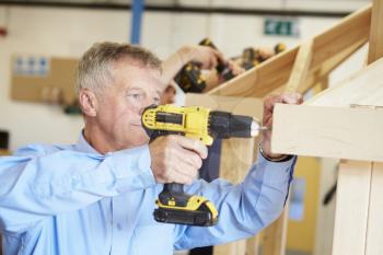 Mature Student Using Drill In Carpentry Class