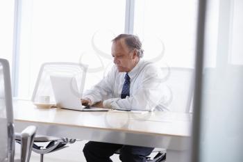 Senior Businessman Working On Laptop At Boardroom Table