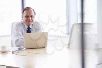 Senior Businessman Working On Laptop At Boardroom Table