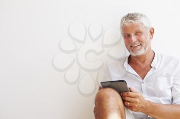 Mature Man Sitting Against Wall Using Digital Tablet