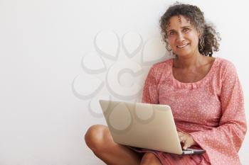 Mature Woman Sitting Against Wall Using Laptop