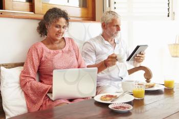 Mature Couple Sitting At Breakfast Table With Digital Devices
