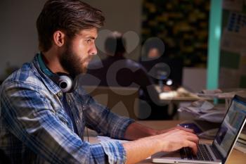 Office Workers At Desks Working Late On Laptops