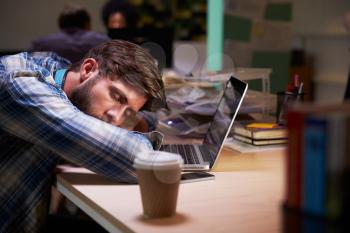 Male Office Worker Asleep At Desk Working Late On Laptop