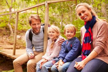Happy family sitting on wooden bridge in a forest, portrait