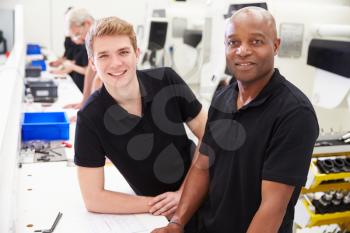 Portrait Of Engineer In Factory With Apprentice At Bench