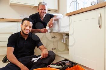 Portrait of plumber with apprentice in domestic kitchen