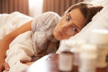 Unhappy Woman Looking At Medication On Bedside Table