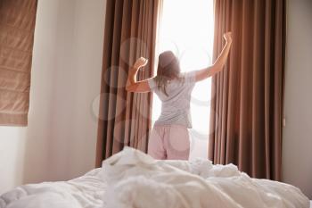 Woman Standing By Bedroom Window In Morning And Stretching