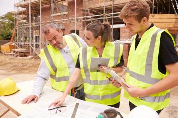 Builder On Building Site Discussing Work With Apprentices