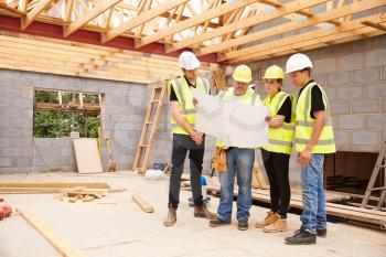 Builder On Building Site Looking At Plans With Apprentices