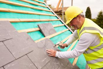Construction Worker On Building Site Laying Slate Tiles