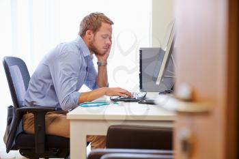 Overworked Male Doctor In Office Sitting At Computer