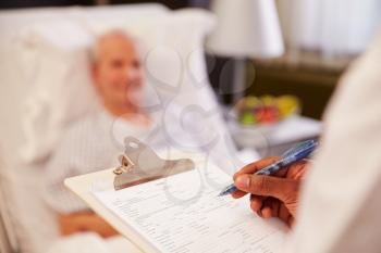Close Up Of Doctor Writing On Senior Male Patient's Chart
