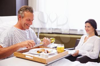 Male Patient In Hospital Bed Eating Meal From Tray