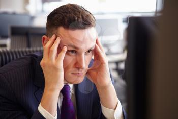 Head and shoulders of a young stressed businessman, head in hands