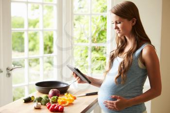 Pregnant Woman Following Recipe On Digital Tablet