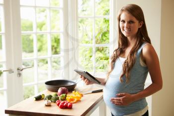 Pregnant Woman Following Recipe On Digital Tablet