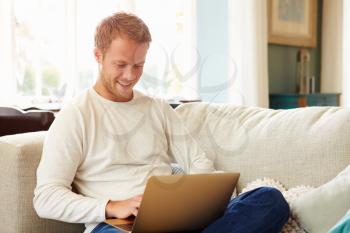 Man Relaxing On Sofa At Home Using Laptop Computer