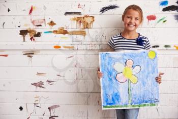 Girl Holding Painting Against Paint Covered Wall In Studio