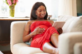 Pregnant Woman On Sofa Relaxing With Digital Tablet