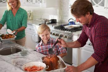 Father And Son Cooking Roast Turkey In Kitchen Together