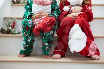 Two Children Sitting On Stairs With Christmas Stockings