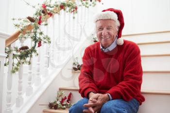 Grandfather Wearing Santa Hat Sitting On Stairs At Christmas