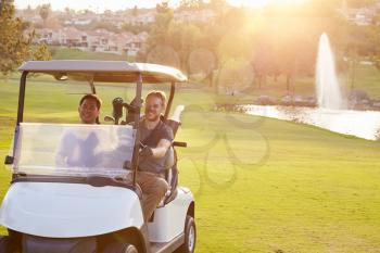 Male Golfers Driving Buggy Along Fairway Of Golf Course