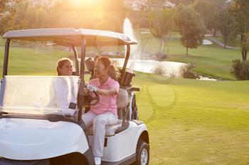 Female Golfers Driving Buggy Along Fairway Of Golf Course