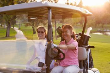 Female Golfers Driving Buggy Along Fairway Of Golf Course