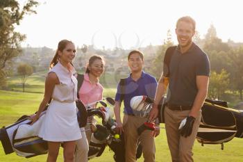 Group Of Golfers Walking Along Fairway Carrying Golf Bags
