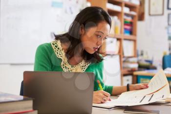 Female Asian teacher at her desk marking students work