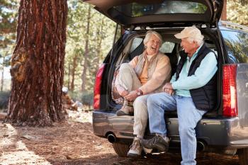 Happy senior couple sit in open car trunk preparing for hike