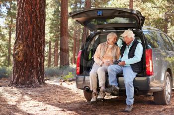 Senior couple sitting in open car trunk preparing for a hike
