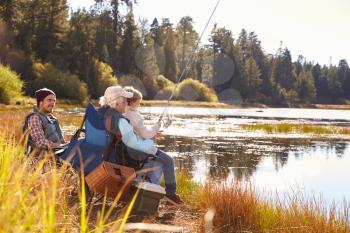 Grandad teaches his grandson to fish at a lake, dad watching