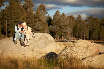 Senior couple sit on a rock near a forest, California, USA