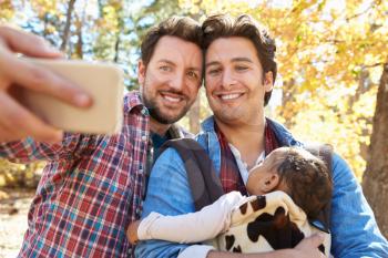 Gay Male Couple With Baby Taking Selfie On Walk In Woodland