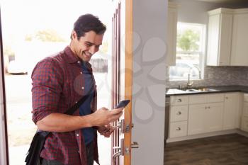 Man Checking Mobile Phone As He Opens Door Of Apartment