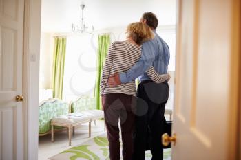 Senior couple arrive embracing in a hotel room, back view