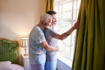 Male couple embrace looking out of their hotel room window