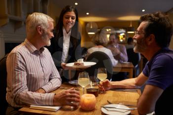 Waitress serving a middle aged male couple in a restaurant